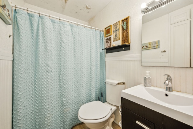 full bath with a shower with shower curtain, a wainscoted wall, toilet, and vanity