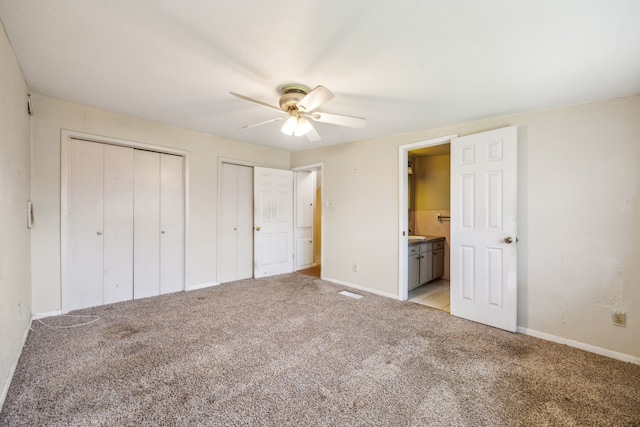 unfurnished bedroom with light carpet, two closets, ensuite bath, and baseboards