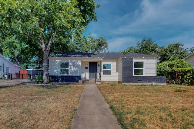 bungalow-style home with brick siding, a front lawn, and fence