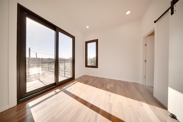 unfurnished room featuring recessed lighting, a barn door, baseboards, and light wood finished floors