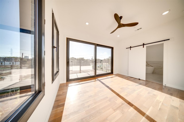 empty room featuring visible vents, a ceiling fan, light wood-style floors, and a barn door