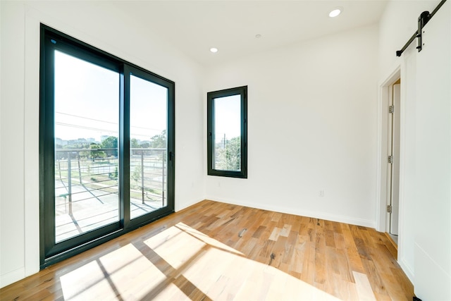 spare room featuring recessed lighting, baseboards, light wood-type flooring, and a barn door