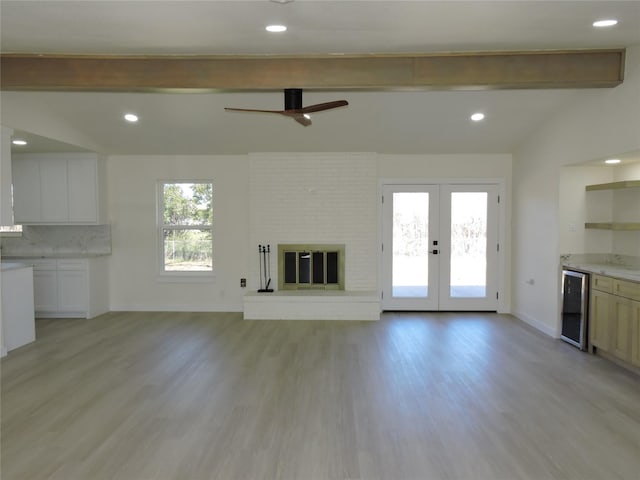 unfurnished living room featuring a brick fireplace, beverage cooler, lofted ceiling with beams, french doors, and light wood-style floors