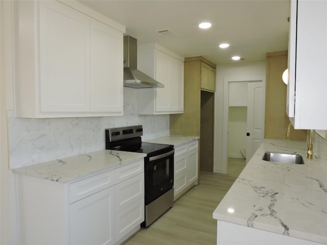 kitchen with a sink, wall chimney range hood, light stone countertops, and stainless steel range with electric cooktop