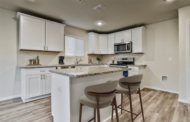 kitchen featuring light wood-style flooring, appliances with stainless steel finishes, white cabinets, and a kitchen breakfast bar