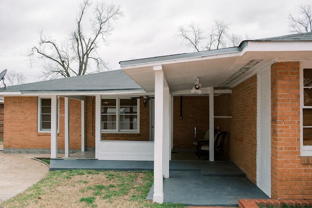 view of exterior entry with brick siding, covered porch, and a shingled roof