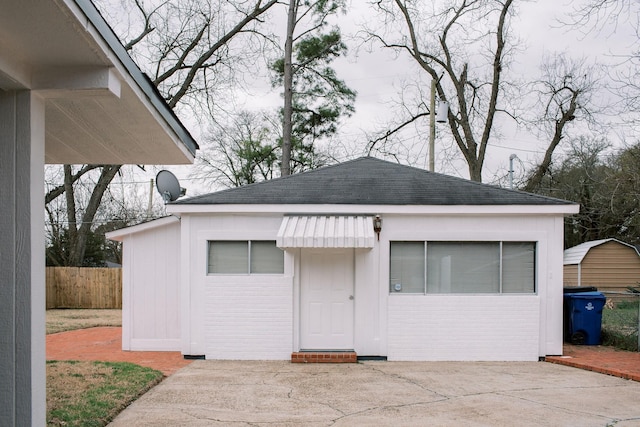 view of front of house with a patio area, a shingled roof, an outdoor structure, and fence