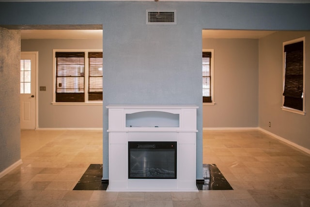 unfurnished living room with visible vents, baseboards, and a glass covered fireplace