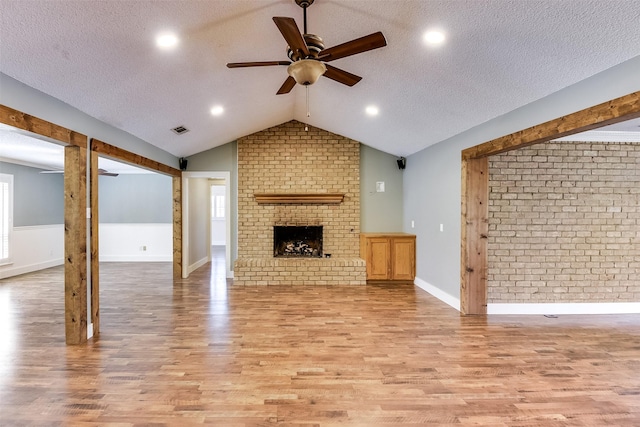 unfurnished living room featuring visible vents, lofted ceiling, a fireplace, a textured ceiling, and light wood-type flooring