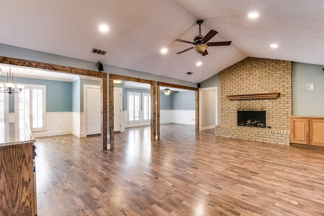 unfurnished living room featuring light wood-type flooring, visible vents, a textured ceiling, a fireplace, and lofted ceiling