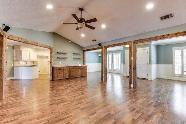 unfurnished living room with vaulted ceiling, a ceiling fan, light wood-style floors, and visible vents