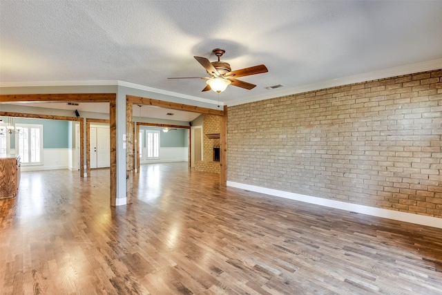 unfurnished room featuring visible vents, a textured ceiling, wood finished floors, and brick wall