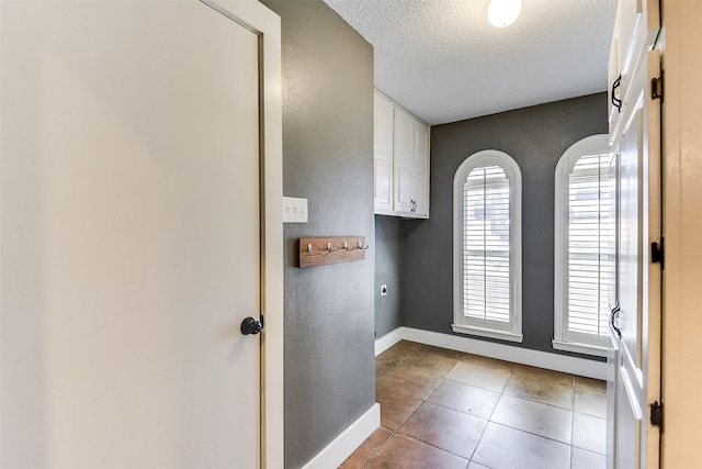 laundry area featuring a textured ceiling, cabinet space, tile patterned flooring, hookup for an electric dryer, and a textured wall