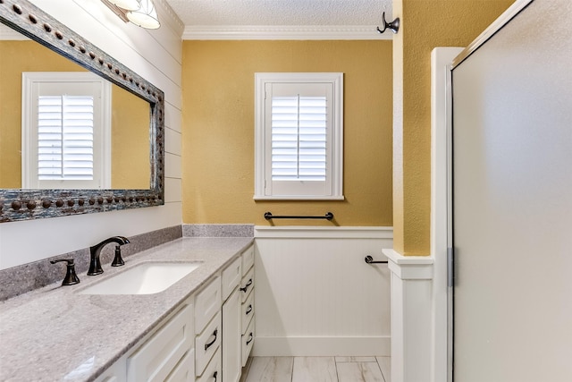 bathroom with a wainscoted wall, vanity, ornamental molding, an enclosed shower, and a textured ceiling