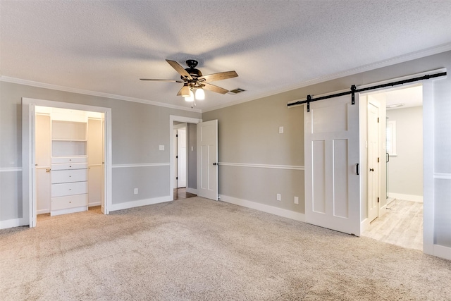 unfurnished bedroom featuring a barn door, a textured ceiling, crown molding, and carpet