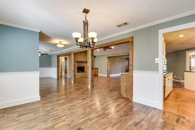 interior space featuring light wood finished floors, visible vents, a brick fireplace, crown molding, and a textured ceiling