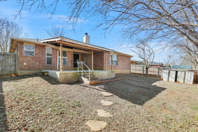 back of house featuring a patio, a fenced backyard, brick siding, and a chimney