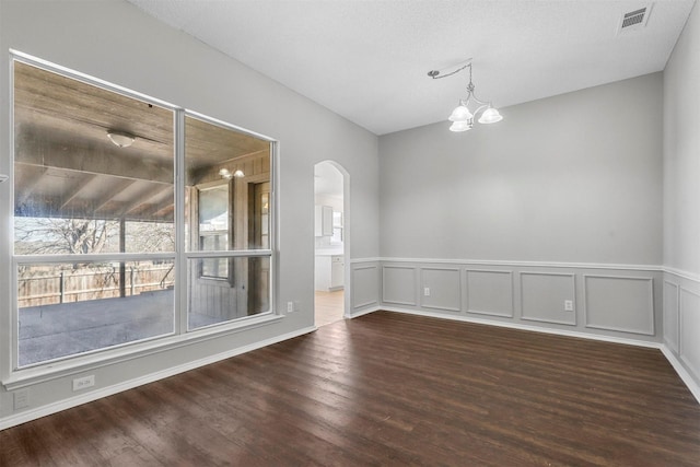 spare room featuring visible vents, arched walkways, a notable chandelier, and wood finished floors