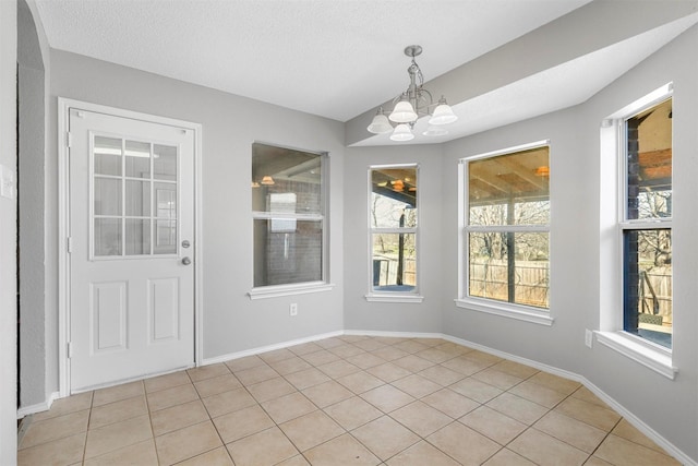 unfurnished dining area with baseboards, a textured ceiling, and an inviting chandelier