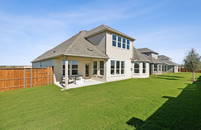 rear view of property featuring brick siding, fence, roof with shingles, a lawn, and a patio area