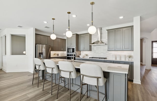 kitchen with arched walkways, a sink, stainless steel appliances, wall chimney exhaust hood, and tasteful backsplash