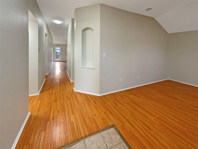 hallway with light wood finished floors, visible vents, lofted ceiling, and baseboards