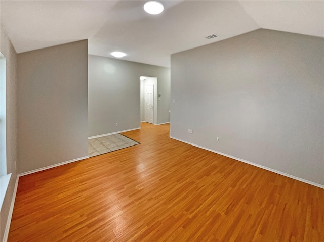 unfurnished room featuring visible vents, lofted ceiling, baseboards, and light wood-style flooring