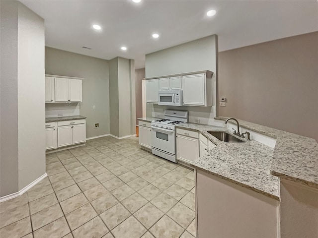 kitchen with light stone countertops, a peninsula, white appliances, white cabinetry, and a sink