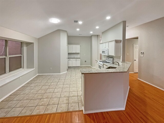 kitchen featuring visible vents, light stone countertops, a peninsula, white appliances, and white cabinetry