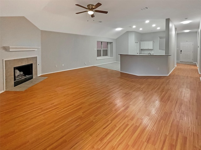 unfurnished living room featuring a ceiling fan, visible vents, a tile fireplace, vaulted ceiling, and light wood-type flooring