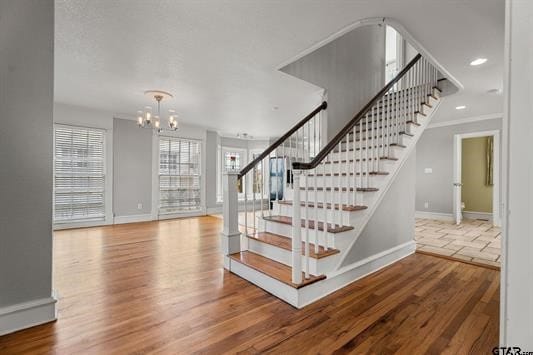 stairs featuring a chandelier, baseboards, wood finished floors, and crown molding