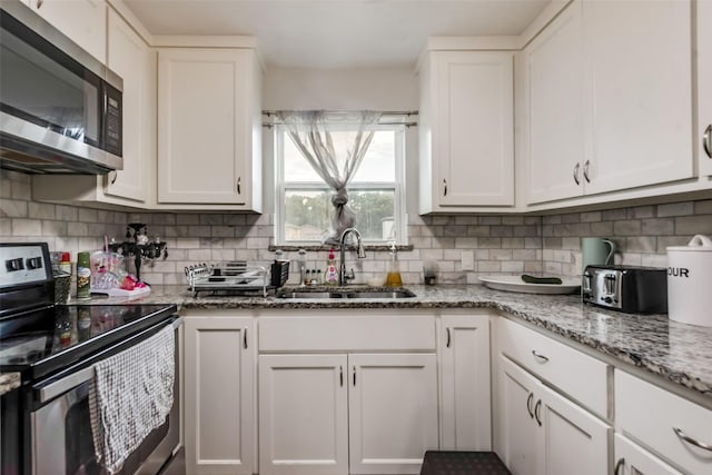 kitchen with backsplash, appliances with stainless steel finishes, white cabinetry, and a sink