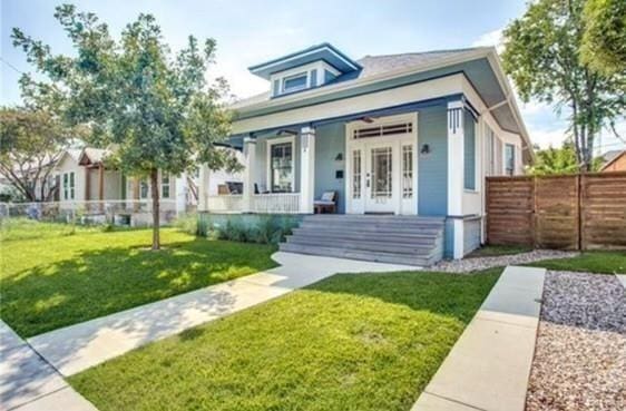 view of front of house with covered porch, french doors, a front lawn, and fence