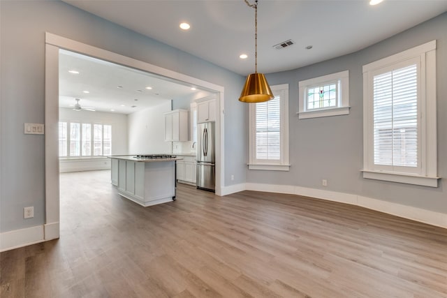 kitchen featuring visible vents, a kitchen island, open floor plan, stainless steel fridge, and white cabinetry