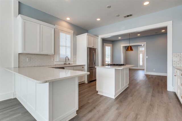 kitchen with visible vents, stainless steel refrigerator, light wood-style floors, white cabinetry, and a center island