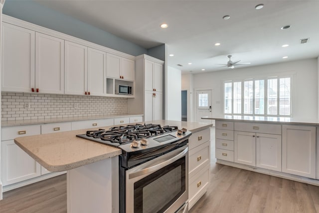 kitchen featuring tasteful backsplash, gas stove, a center island, and light wood-style floors