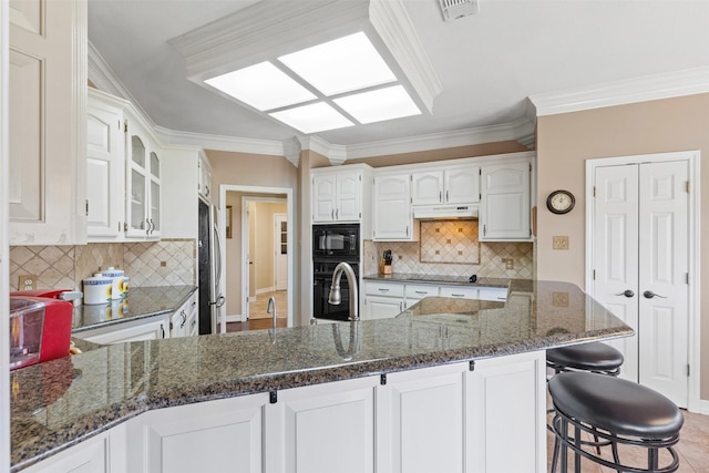 kitchen featuring visible vents, black appliances, dark stone counters, a peninsula, and white cabinetry