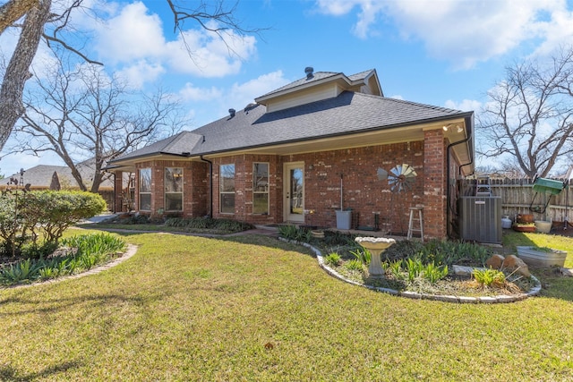 rear view of house with a lawn, fence, cooling unit, a shingled roof, and brick siding