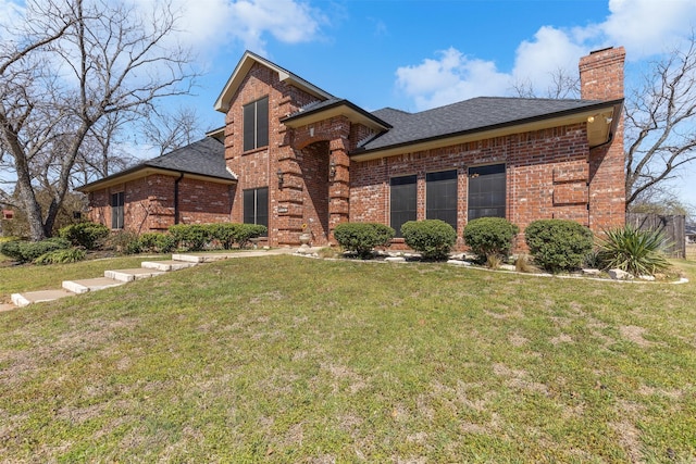 view of front of house featuring brick siding, a chimney, a shingled roof, and a front yard