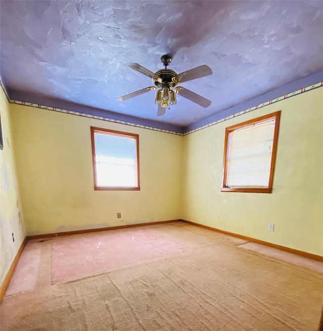 carpeted spare room with a ceiling fan and baseboards