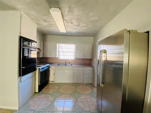 kitchen featuring electric stove, a sink, black oven, white cabinetry, and freestanding refrigerator