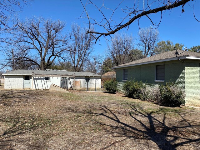 view of property exterior featuring brick siding, an outdoor structure, and fence