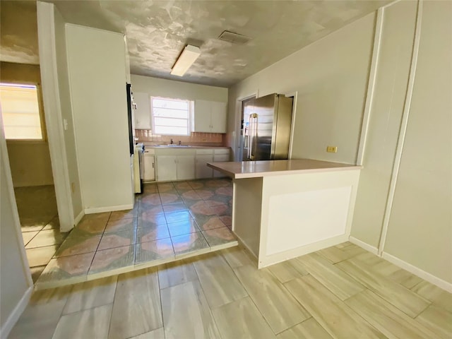 kitchen with high end fridge, a sink, white cabinetry, a peninsula, and light countertops