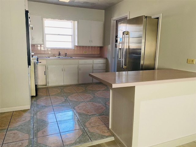 kitchen with backsplash, light countertops, high end refrigerator, white cabinetry, and a sink