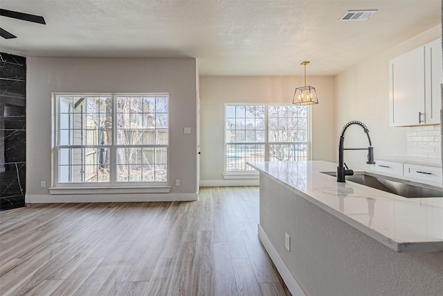 kitchen featuring light wood finished floors, light stone countertops, a textured ceiling, white cabinetry, and a sink