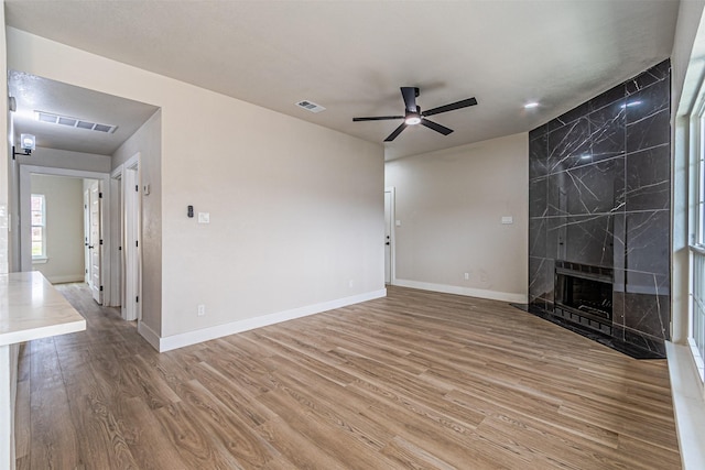 unfurnished living room featuring visible vents, a ceiling fan, wood finished floors, a premium fireplace, and baseboards