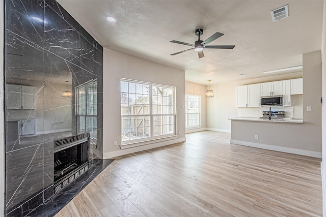 unfurnished living room featuring light wood-type flooring, visible vents, a ceiling fan, a high end fireplace, and baseboards