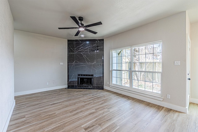 unfurnished living room with baseboards, a ceiling fan, wood finished floors, and a fireplace