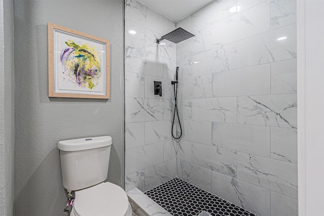 full bath featuring toilet, tiled shower, and a textured wall