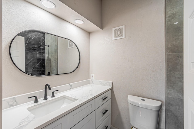 bathroom with vanity, toilet, a textured wall, and walk in shower